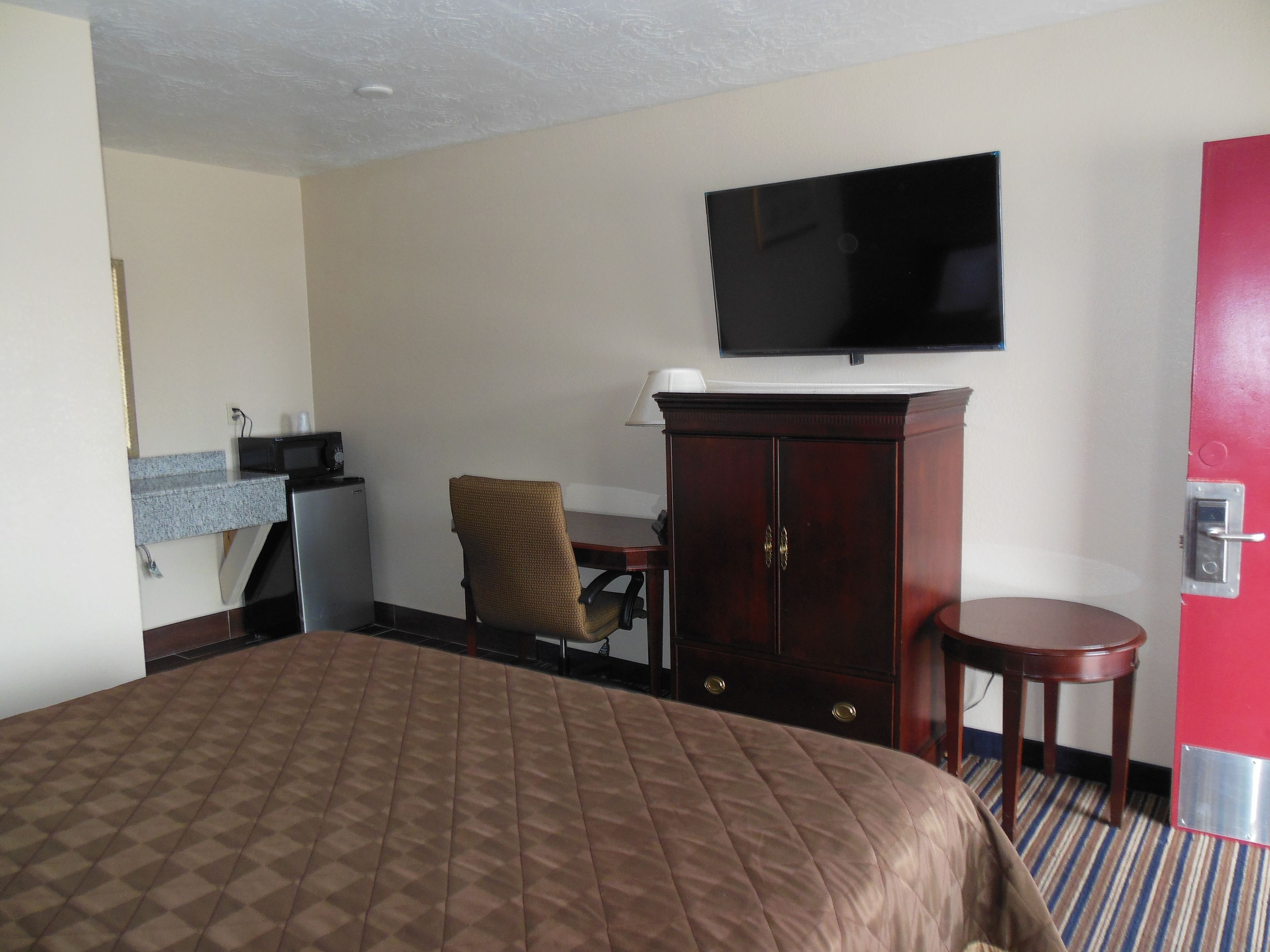 Een hotelkamer met een groot bed, een aan de muur bevestigde televisie, een klein bureau met stoel en een kast.