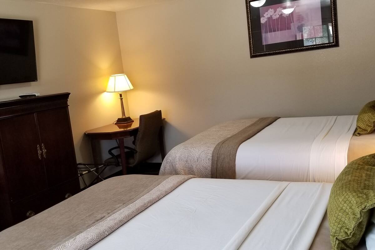 Una habitación de hotel con dos camas, un escritorio, una silla, un televisor y una lámpara.