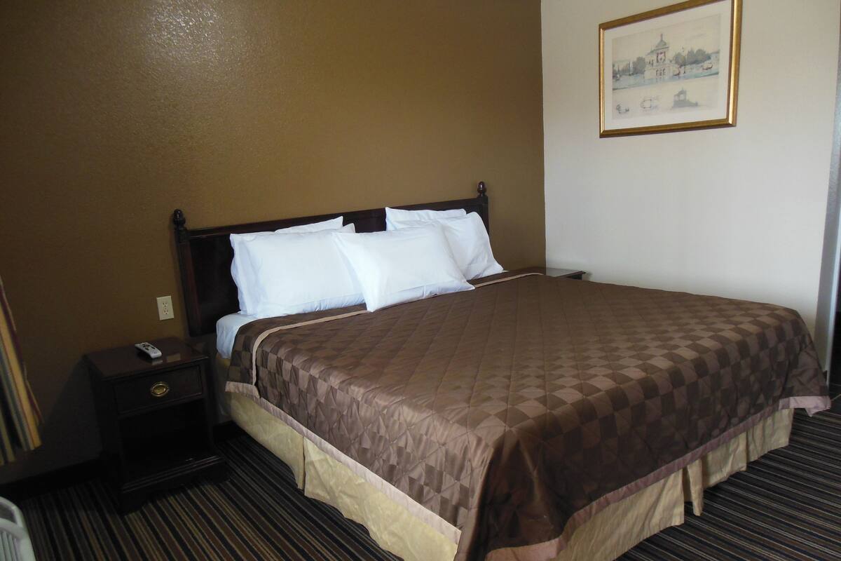 Una habitación de hotel con una cama grande, una mesita de noche, un control remoto y un cuadro en la pared.