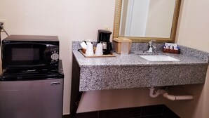 A kitchenette with a microwave, coffee maker, and a countertop with cups and a basket.