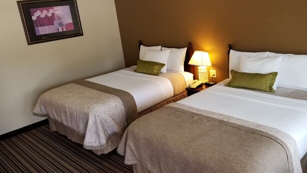 A hotel room with two beds, each with white linens and green pillows, a bedside table with a lamp, and a framed picture on the wall.