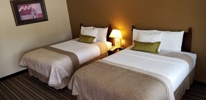 A hotel room with two beds, each with white linens and green pillows, a bedside table with a lamp, and a framed picture on the wall. - Route 66 Inn (Amarillo)
