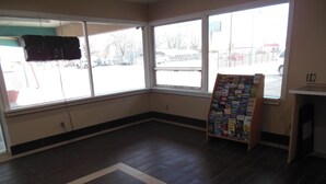 A room with large windows, a dark wooden floor, and a bulletin board with various items.