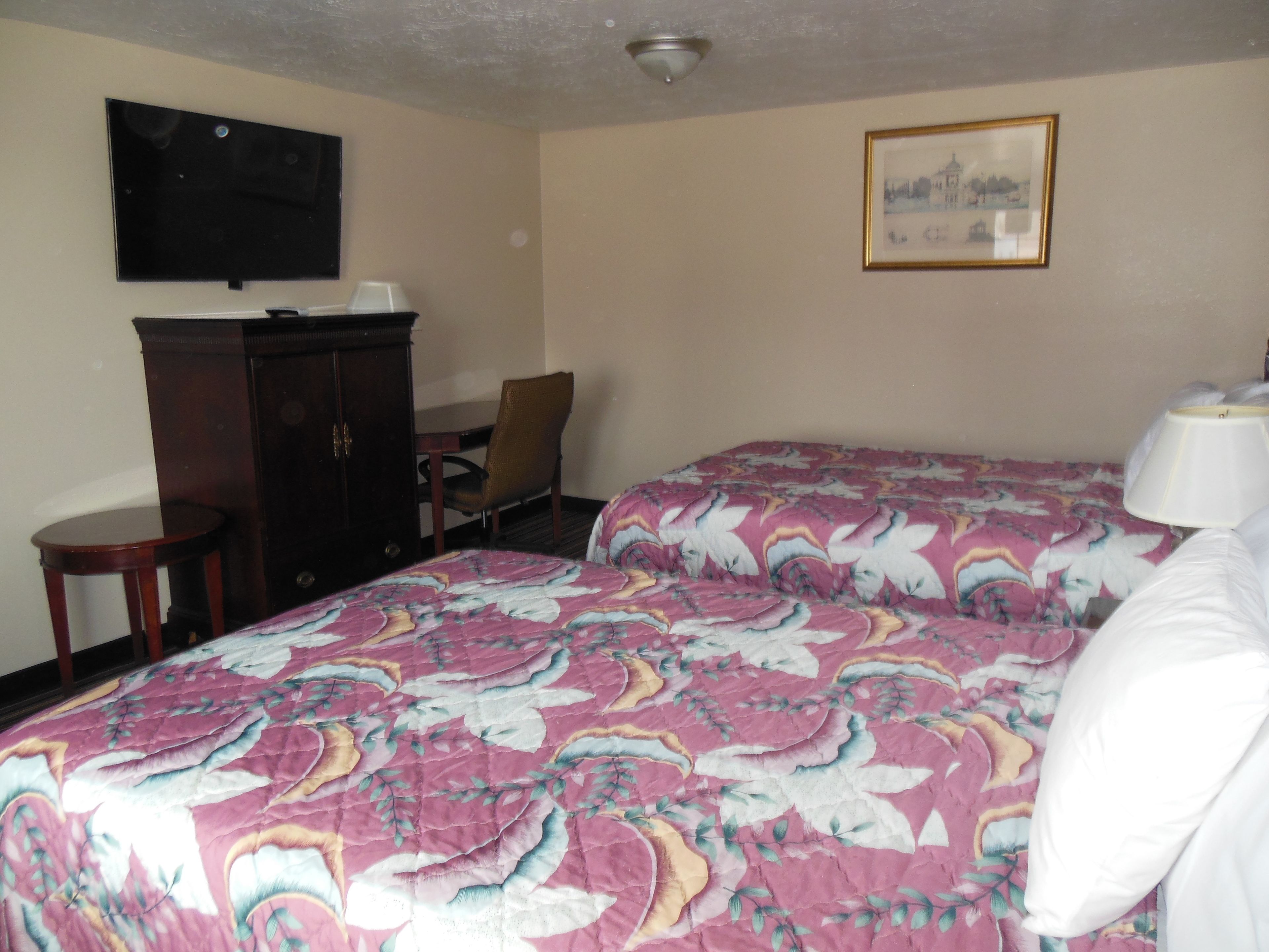 A hotel room with two beds, a desk, a chair, a TV, and a framed picture on the wall.