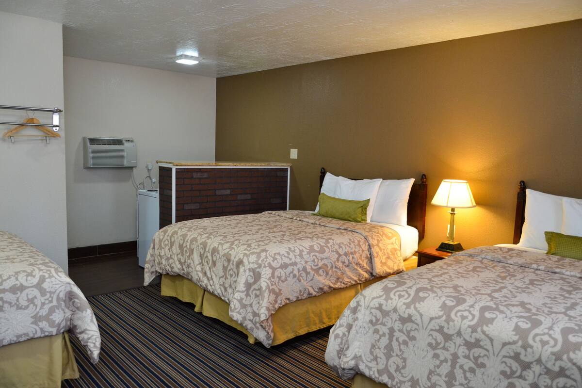 Habitación de hotel con dos camas, una mesita de noche con lámpara, aire acondicionado instalado en la pared y un escritorio pequeño con silla.
