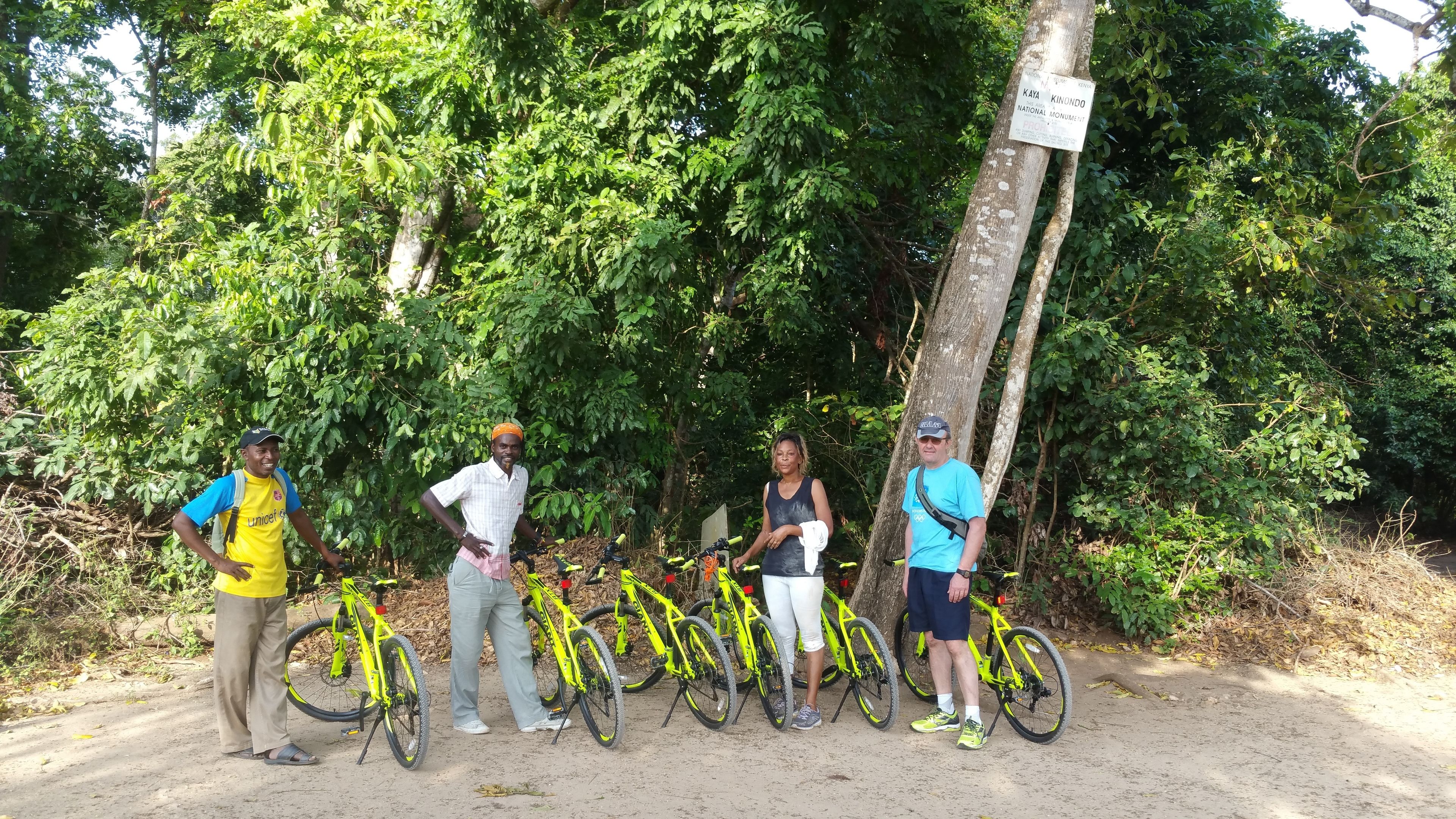 Quatre personnes se tiennent près de vélos dans un cadre naturel, à proximité d’un panneau indiquant un monument national.