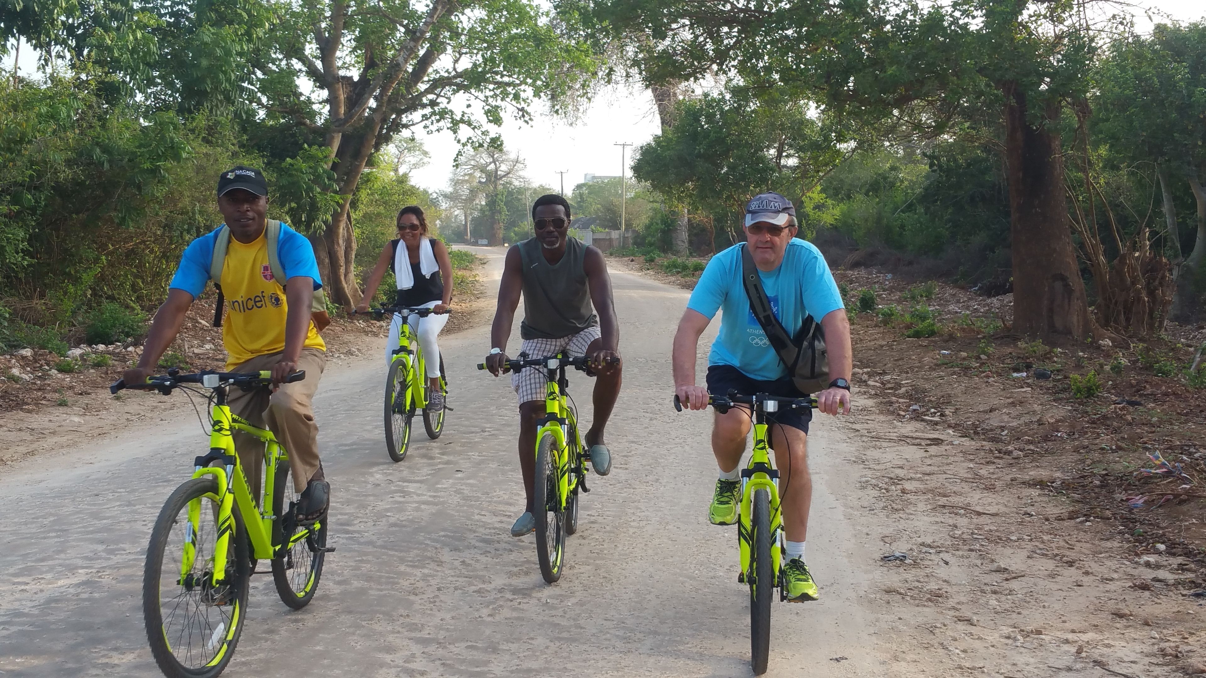 Quatre personnes font du vélo sur un chemin de terre, entourées d’arbres.