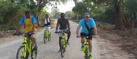 Four people riding bicycles on a dirt road surrounded by trees.