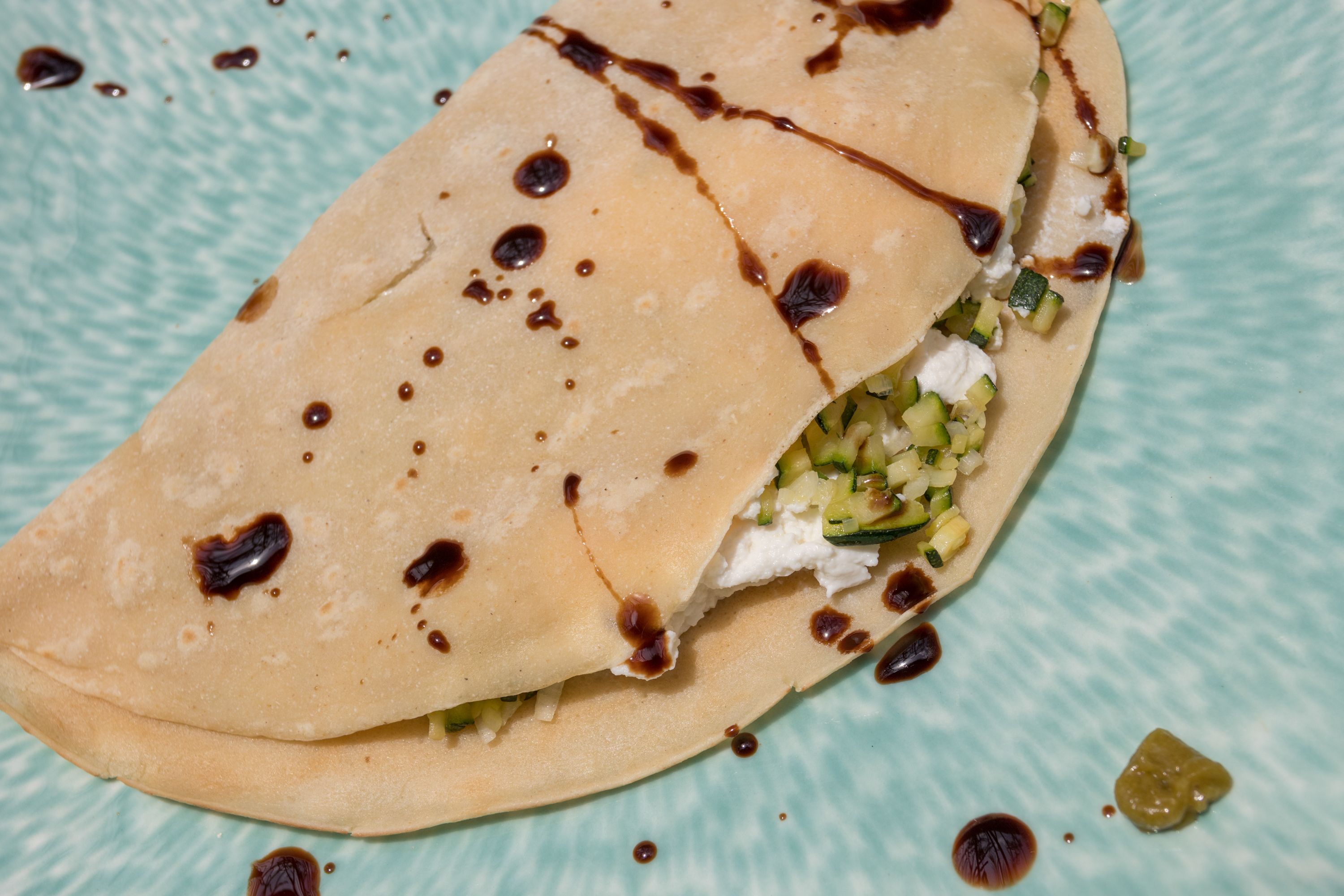 A folded crepe with a filling of cheese and vegetables, drizzled with syrup, on a textured blue plate.