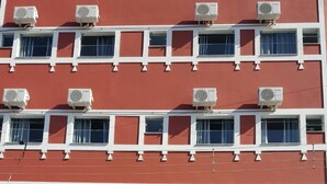A multi-story building with air conditioning units on each floor, a garage entrance, and a person standing near the entrance. - Hotel Pousada do Papa (Aparecida)