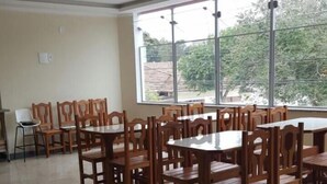 A dining area with wooden tables and chairs, large windows, and a tiled floor. - Hotel Pousada do Papa (Aparecida)