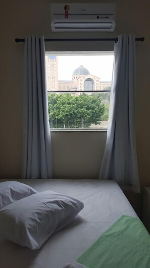 A hotel room with a bed, white curtains, and an air conditioning unit. - Hotel Pousada do Papa (Aparecida)