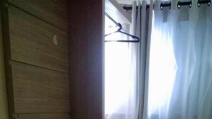 A small room with a wooden wardrobe, a white cabinet, a window with white curtains, and a tiled floor. - Hotel Pousada do Papa (Aparecida)