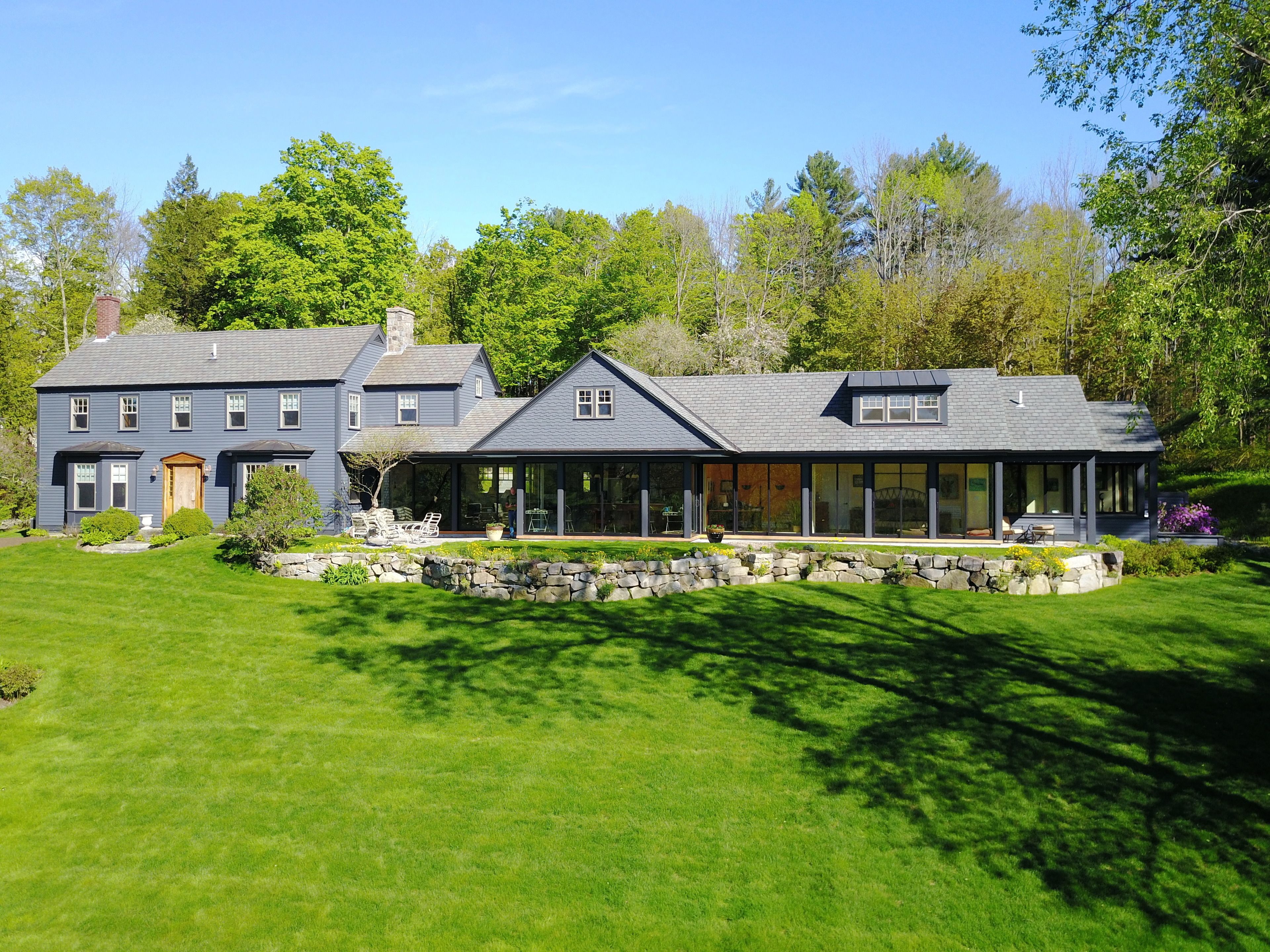 A two-story house with a stone foundation, large windows, and a well-maintained lawn.