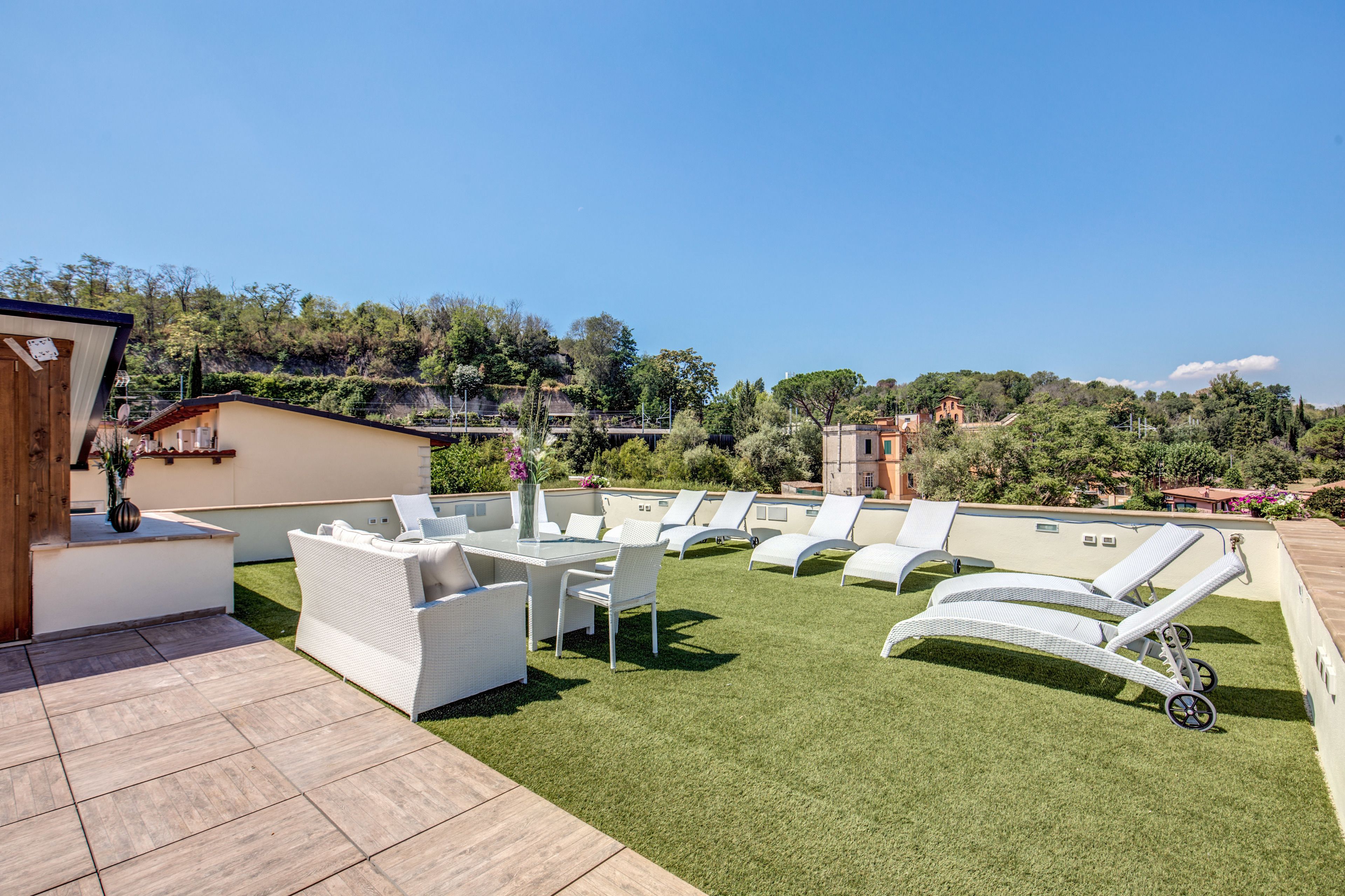 A rooftop terrace with white lounge chairs, a dining table, and a small seating area.