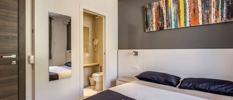 A modern hotel room with a large bed, a bathroom, and a colorful abstract painting on the wall.