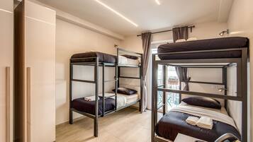 A dormitory-style room with bunk beds, a desk with a telephone, and a window with curtains.