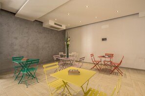 A modern room with a yellow table, green and red chairs, and a grey wall. - The Bricks Rome (Rome)