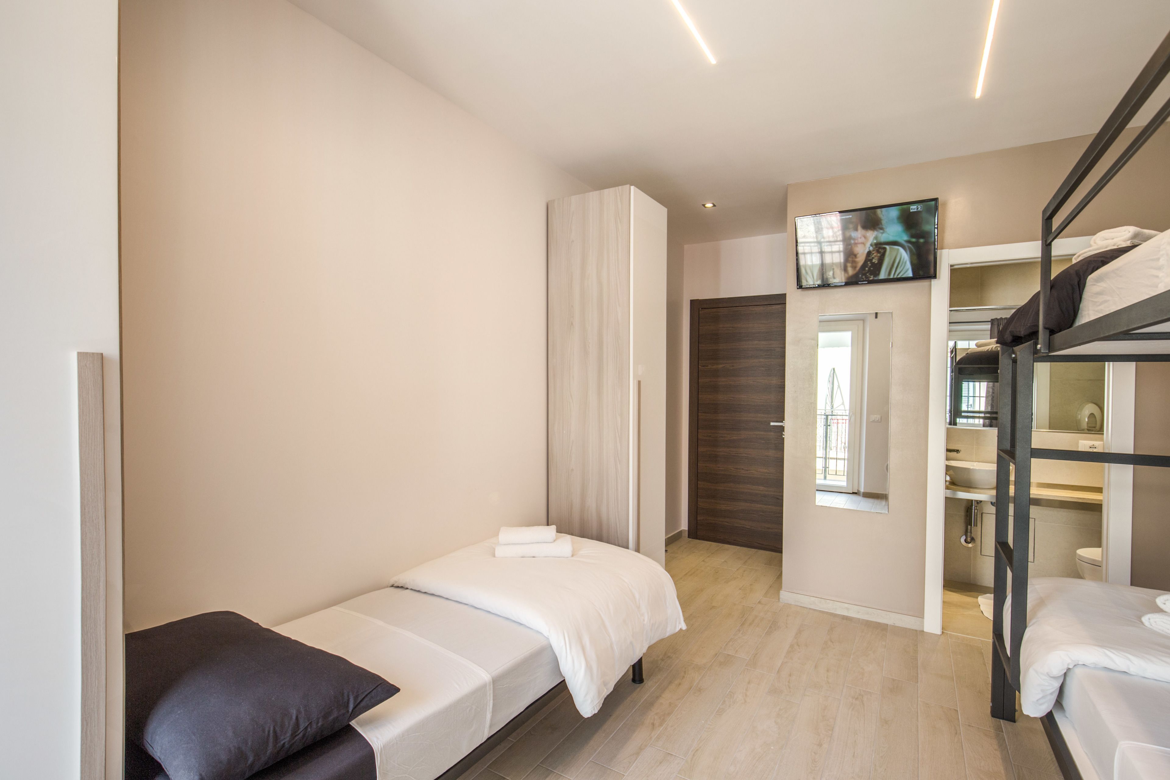 A modern hotel room with a single bed, a small desk, a TV, and a bunk bed.