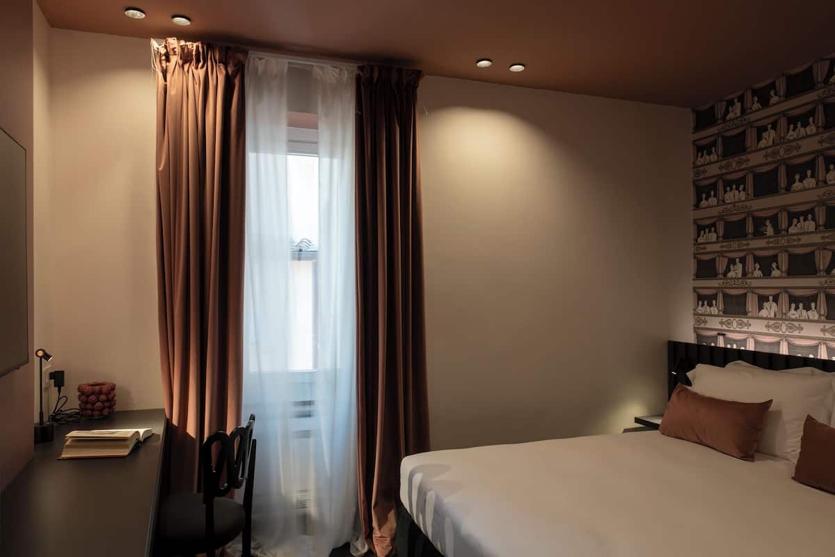 A hotel room with a bed, a desk with a lamp, and a wall with a patterned design.