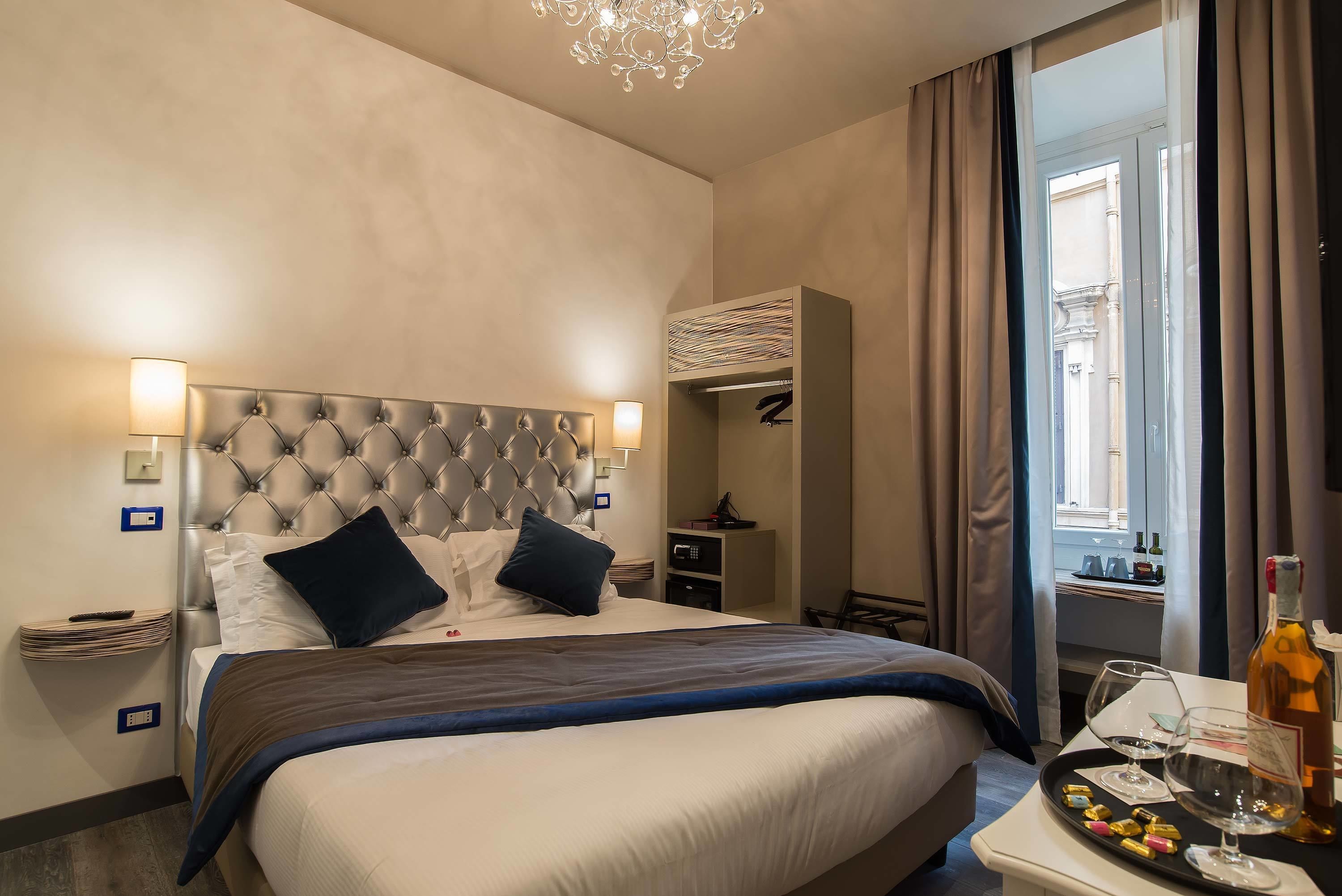 Ein Hotelzimmer mit einem großen Bett, Nachttischlampen, einer Minibar und Blick auf die Stadt.