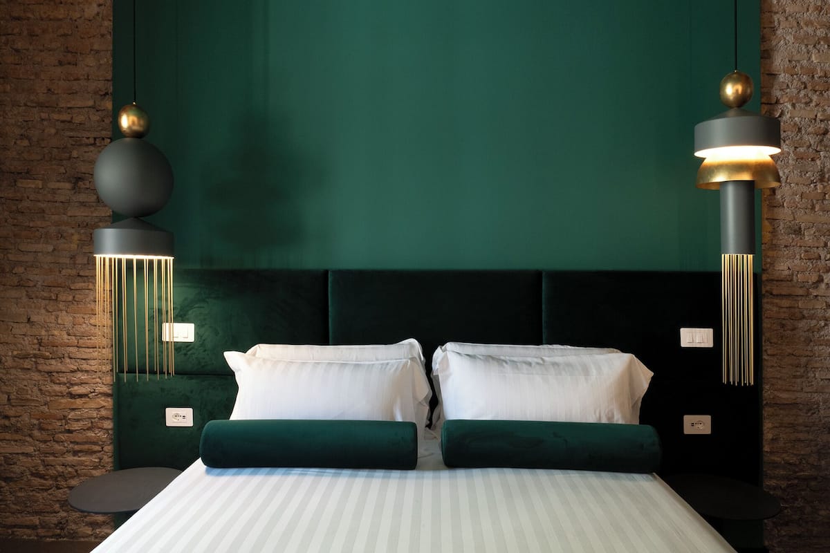 A hotel room with a large bed, two green upholstered headboards, and two wall-mounted pendant lights.