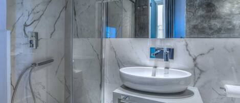 A modern bathroom with a glass-enclosed shower, a white sink with a marble countertop, and a large mirror above the sink.