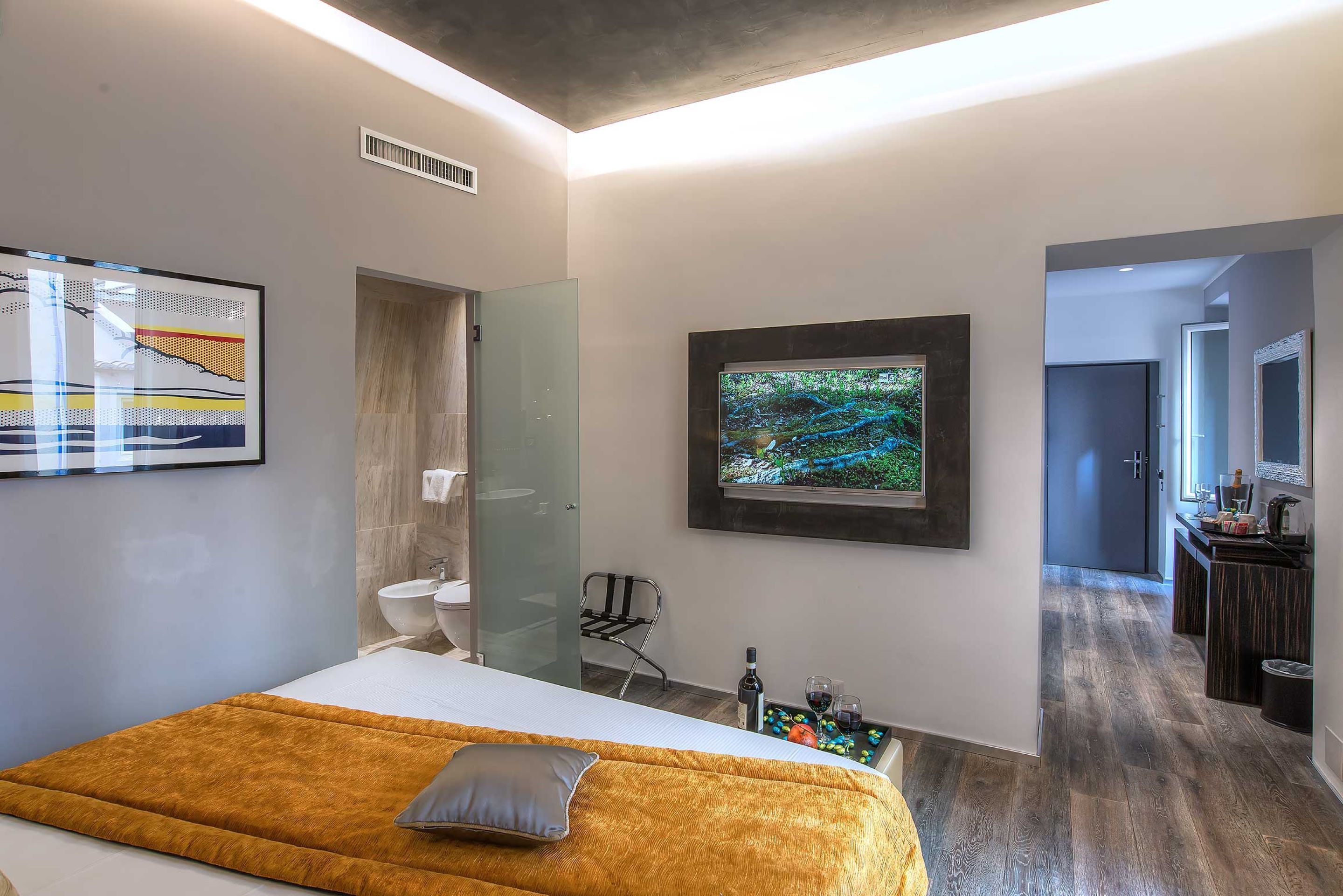 A modern hotel room with a bed, a bathroom, a TV, and a dining area.