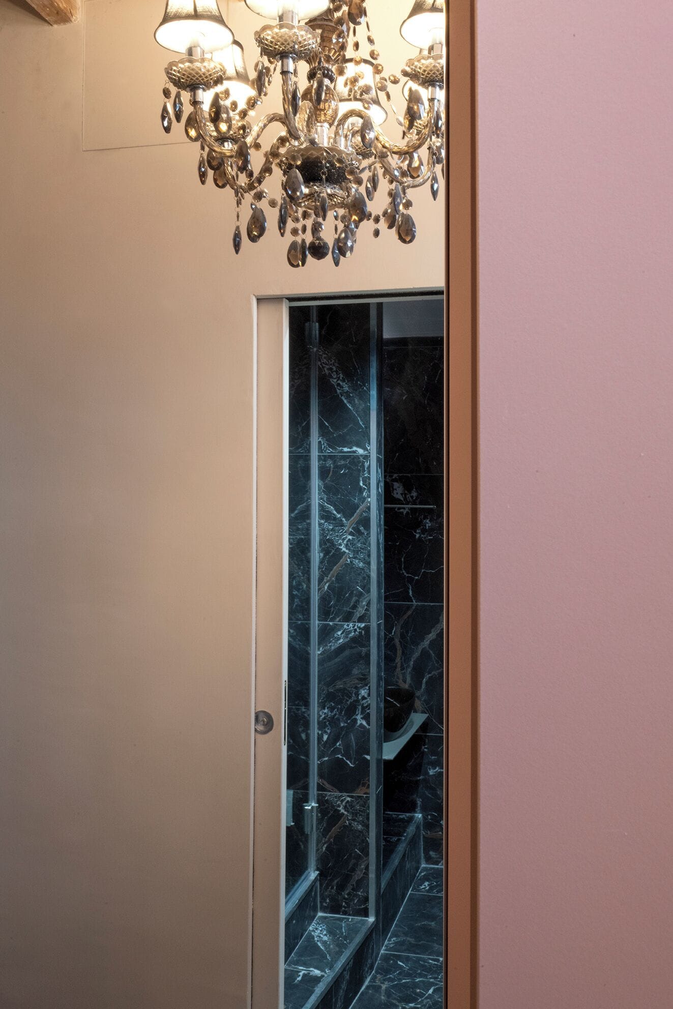 A hallway with a marble wall and a glass elevator door.