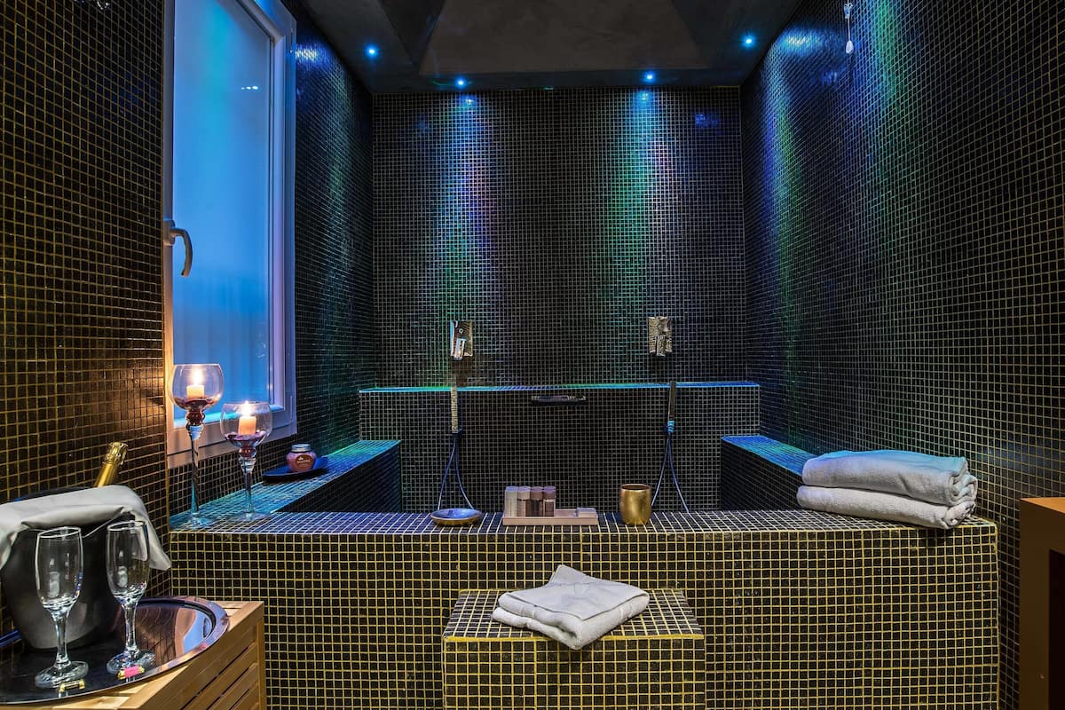A spa room with a tiled wall, a bench, a towel, and a glass of wine.