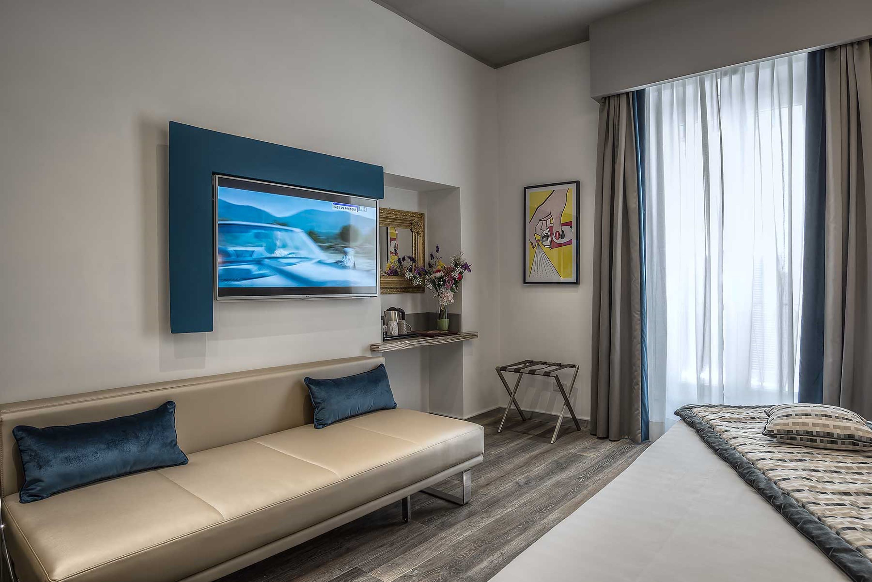 Een moderne hotelkamer met een bank, een bed, een aan de muur bevestigde televisie en een raam met gordijnen.