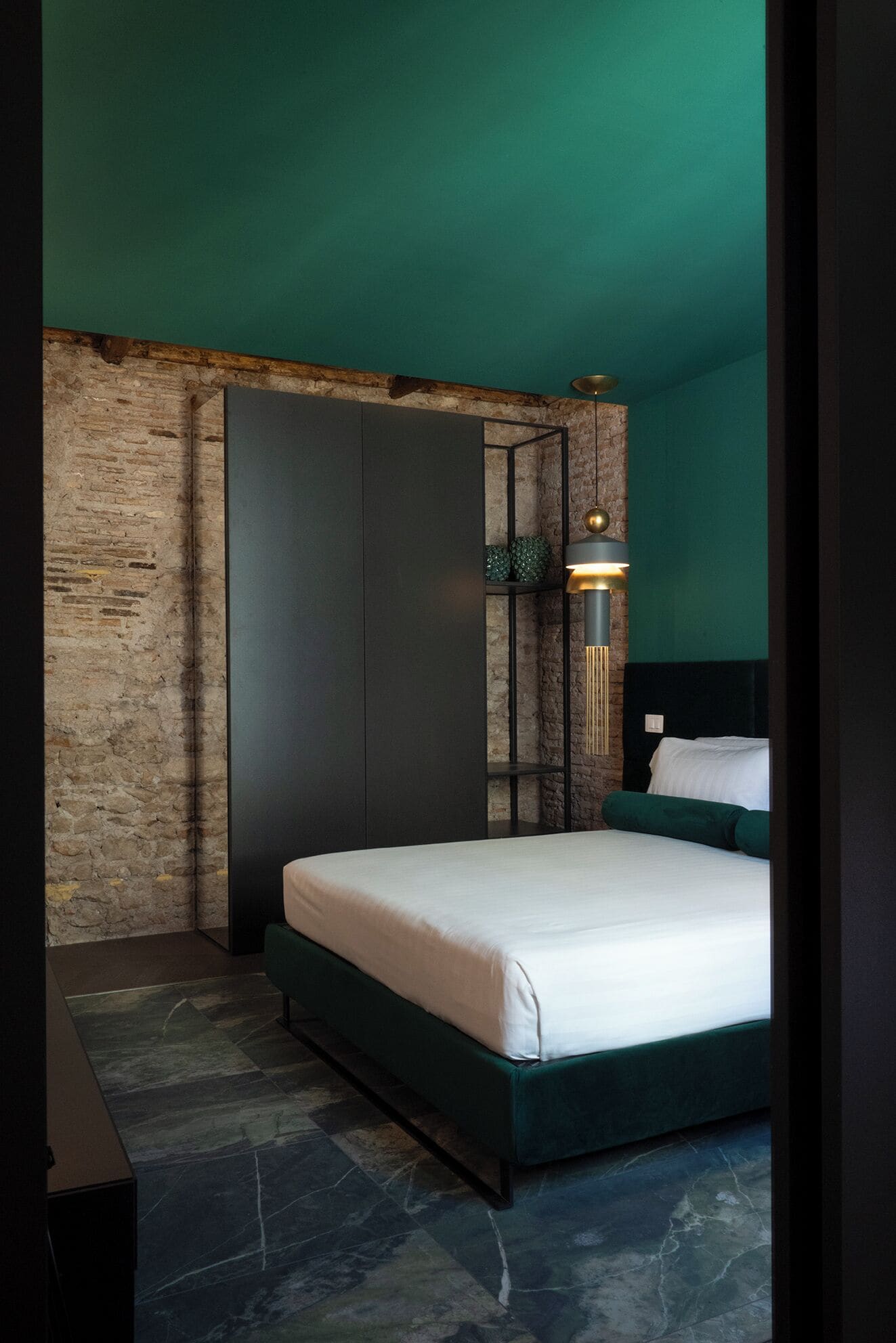 A modern bedroom with a stone wall, a bed with a green headboard, and a unique lighting fixture.