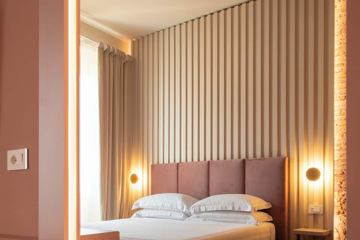 A modern hotel room with a large bed, a nightstand, and a mirror reflecting the room.