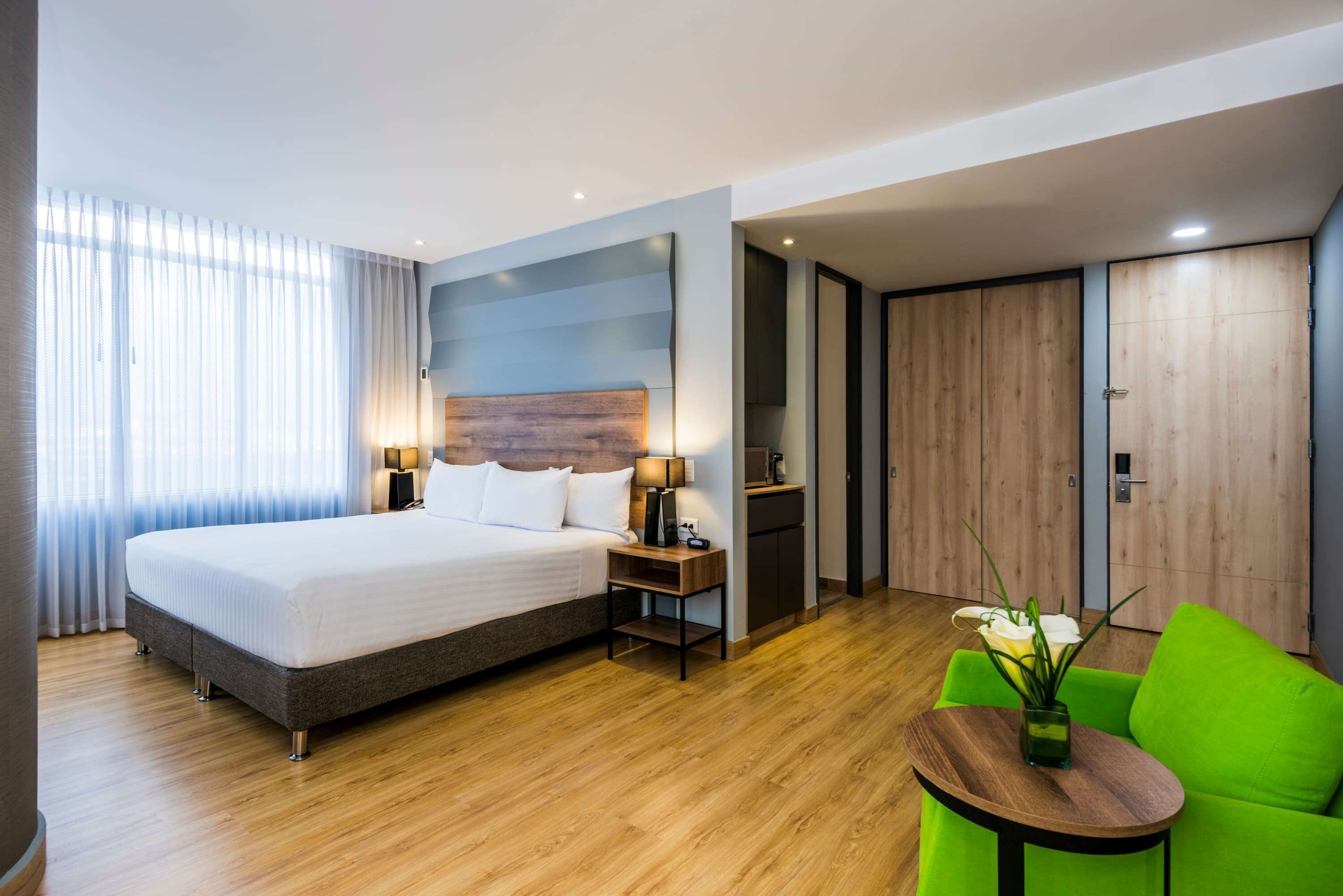 Ein Hotelzimmer mit einem großen Bett, Nachttischen, einem grünen Sessel und einem kleinen Tisch mit einer Vase.