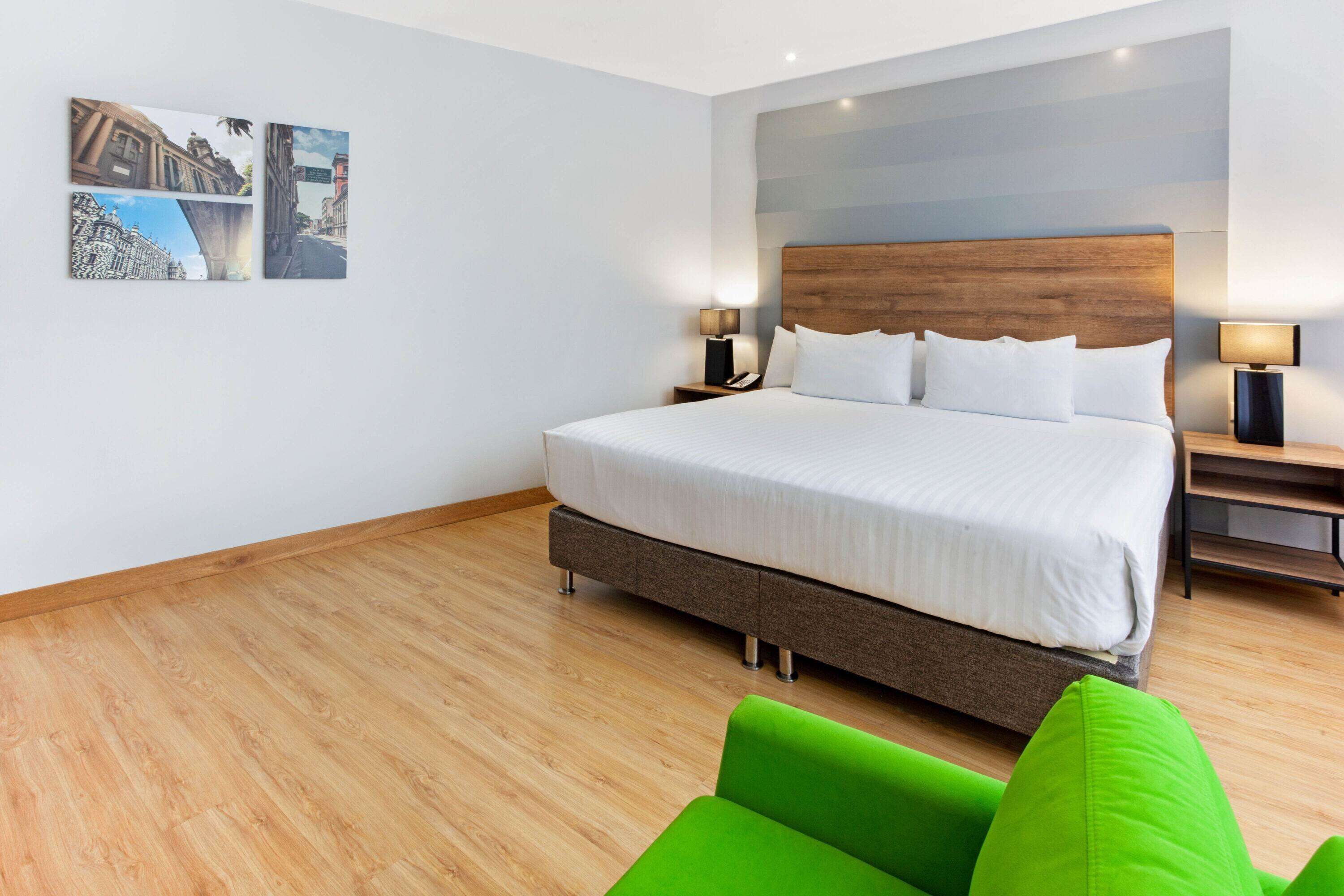 Una habitación de hotel moderna con una cama grande, cabecera de madera y dos mesitas de noche con lámparas.