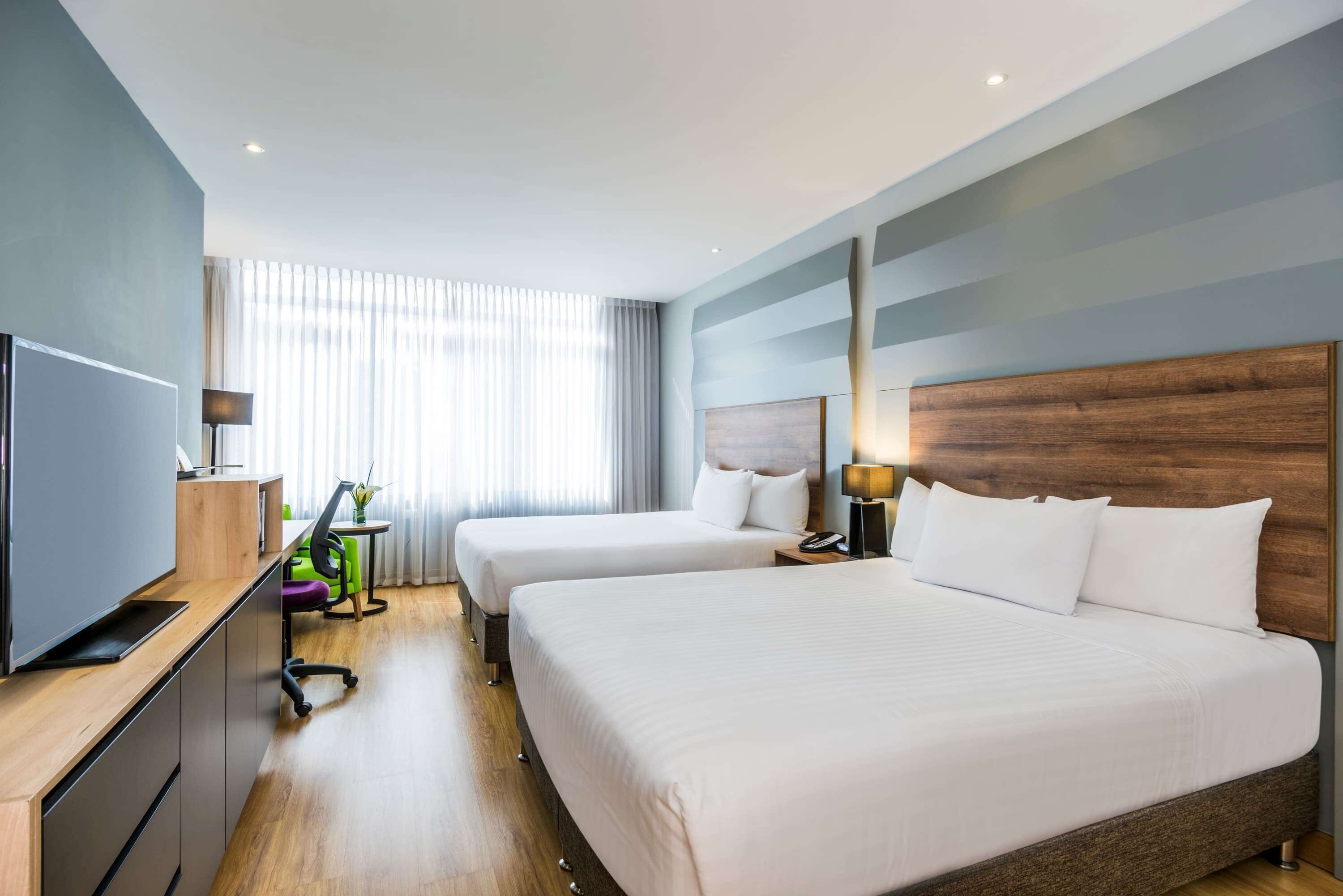 A hotel room with two beds, a TV, a desk, and a chair.