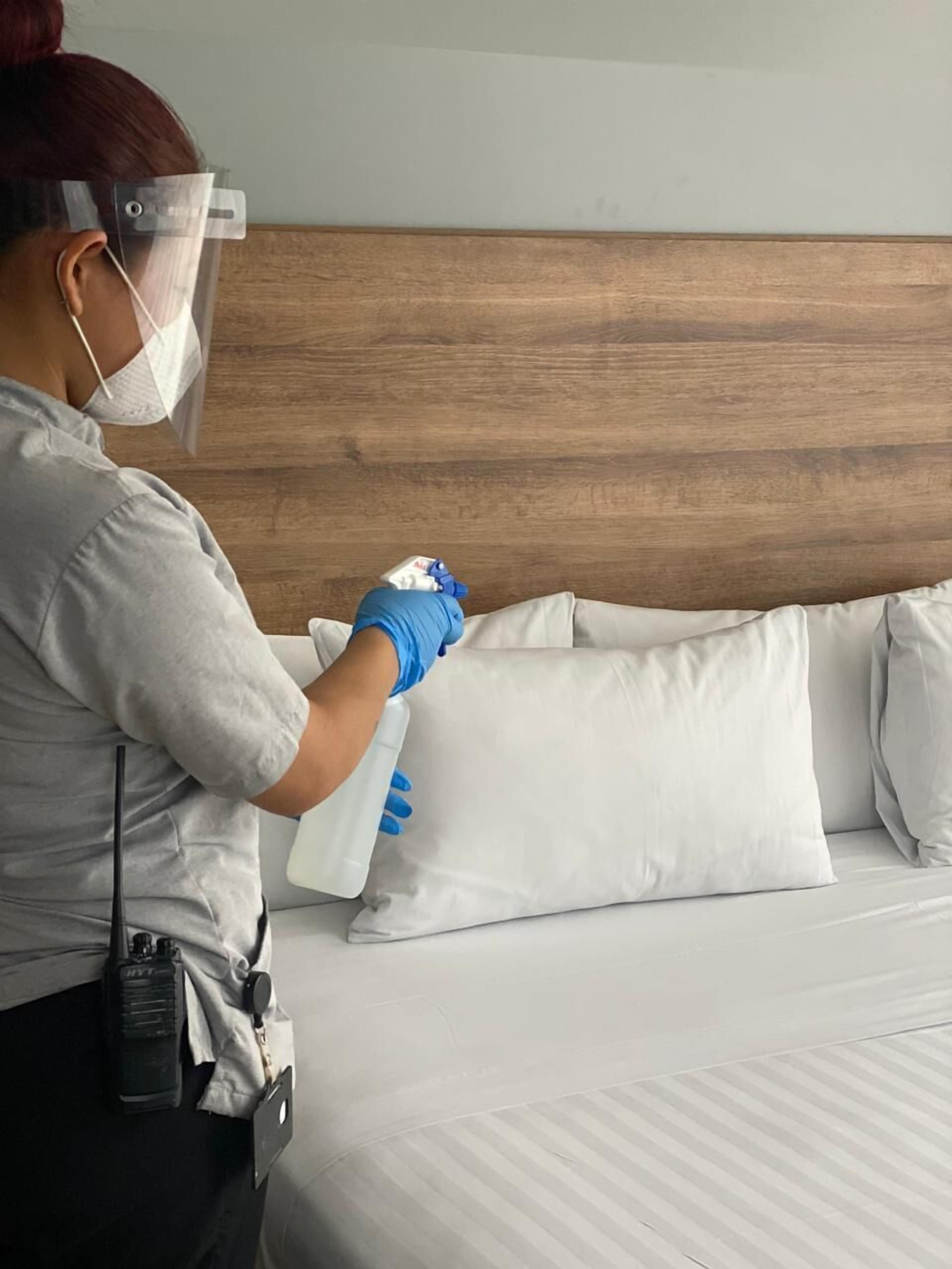 A person cleaning a bed with white pillows and a wooden headboard.