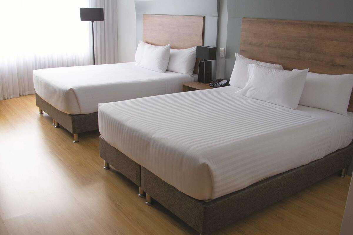 A hotel room with two beds, a bedside table with a lamp, and a nightstand with a phone.