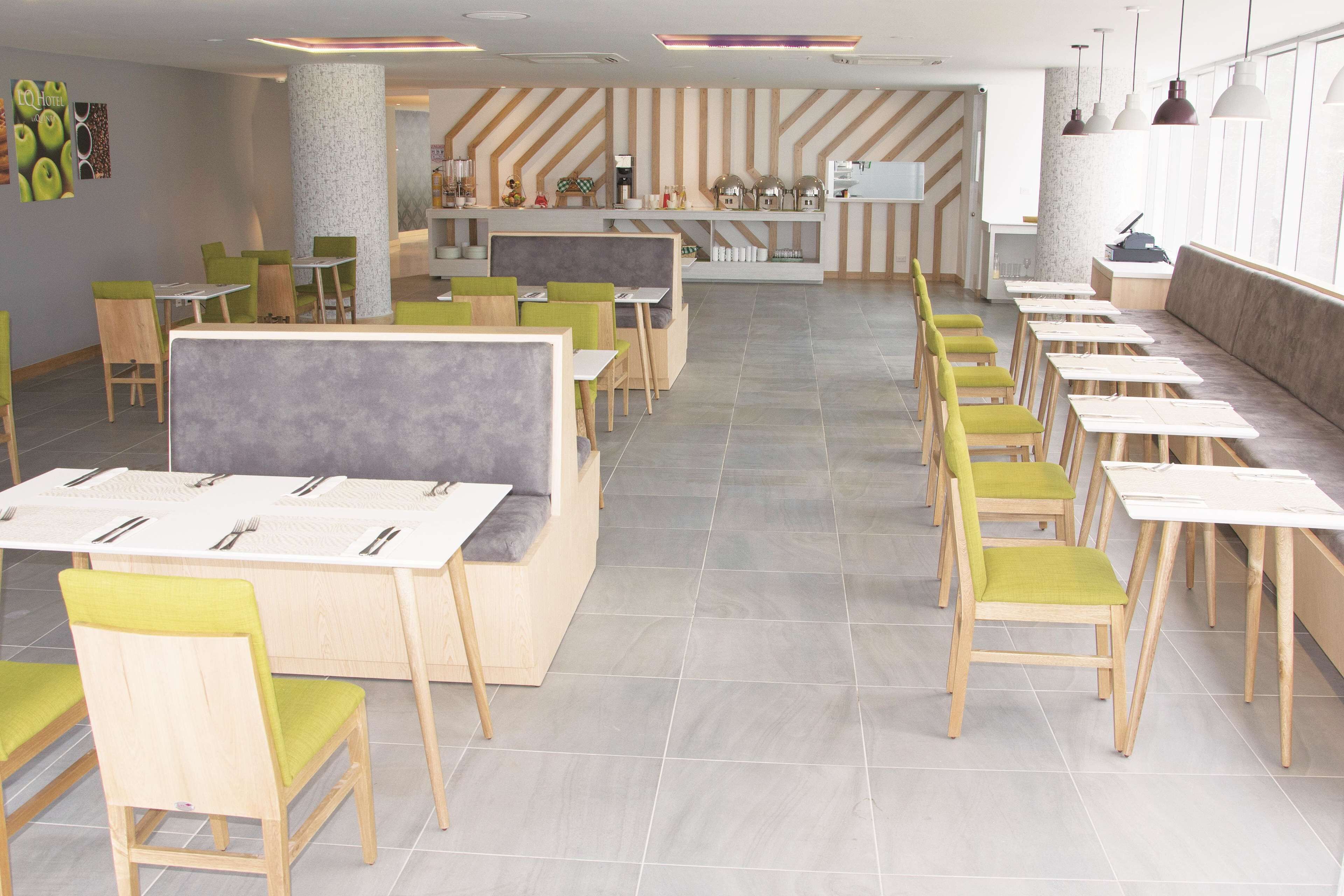 A modern restaurant with long communal tables and booths, green and wooden chairs, and a striped wall design.