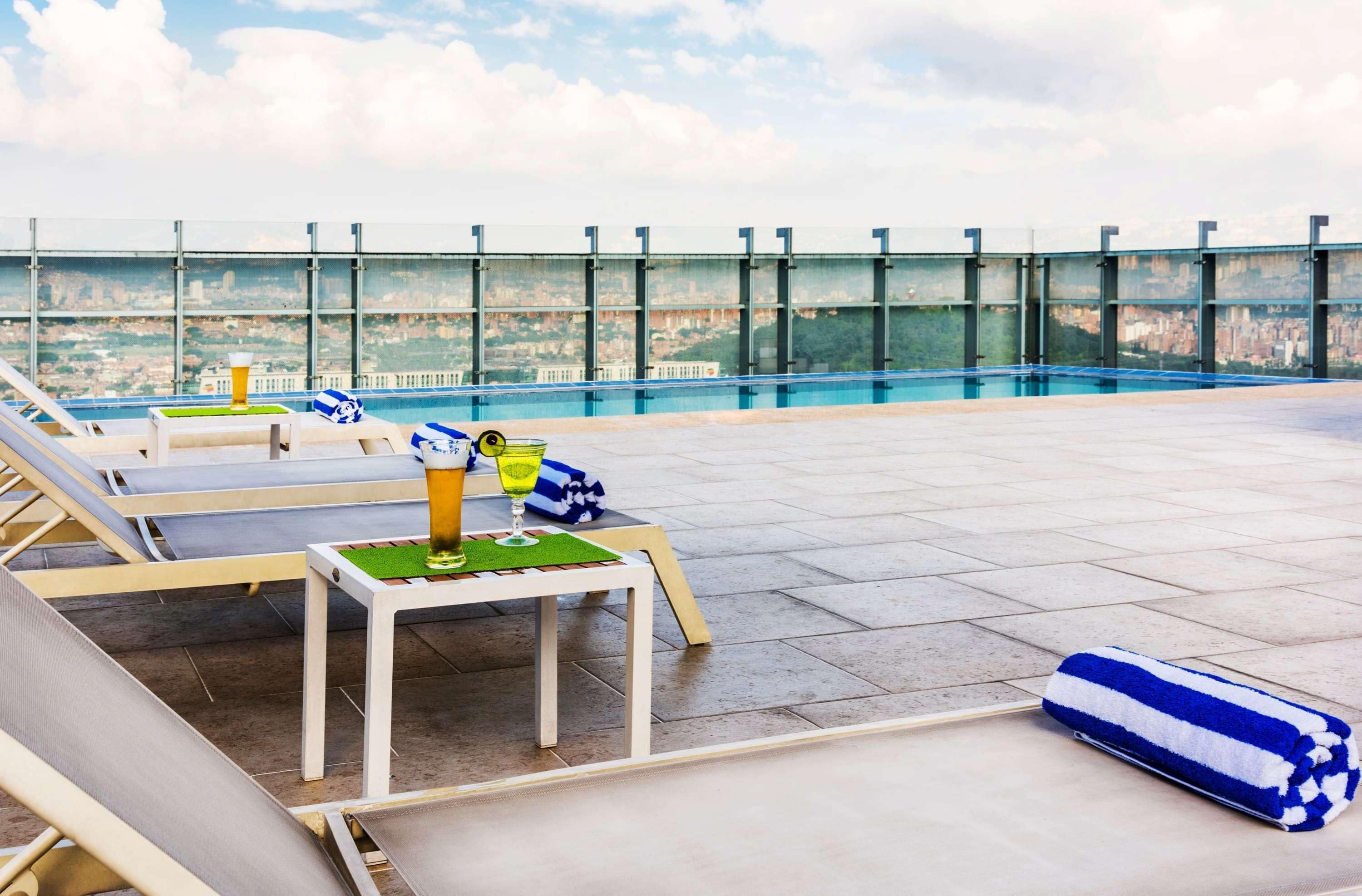 A rooftop pool area with lounge chairs, a table with a drink, and a towel.