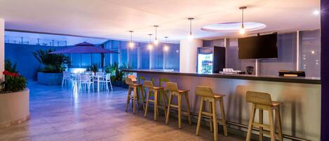 A modern bar area with a counter, bar stools, and a television screen.