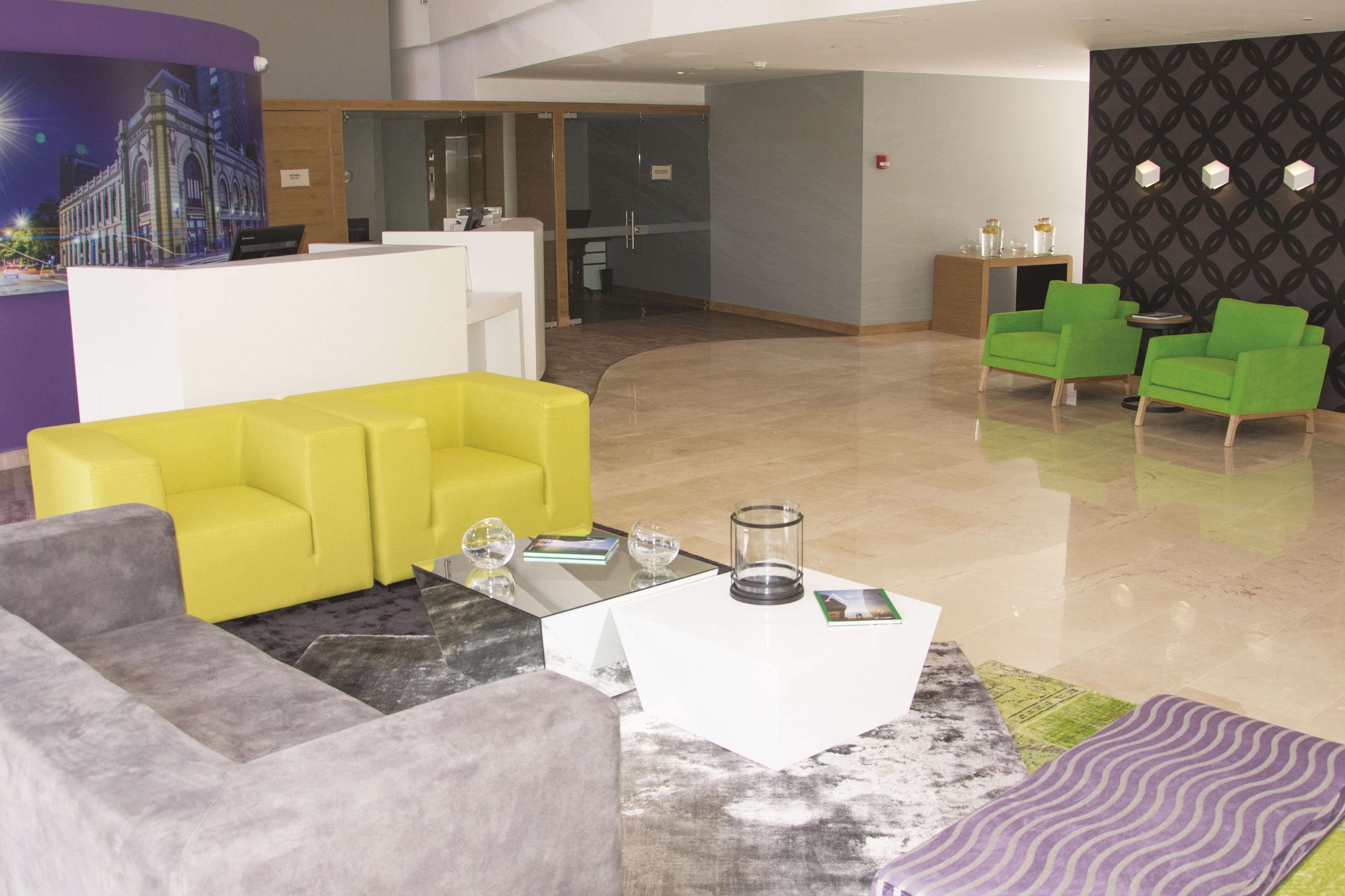 A modern lobby with a reception desk, yellow and gray seating, and a patterned wall.
