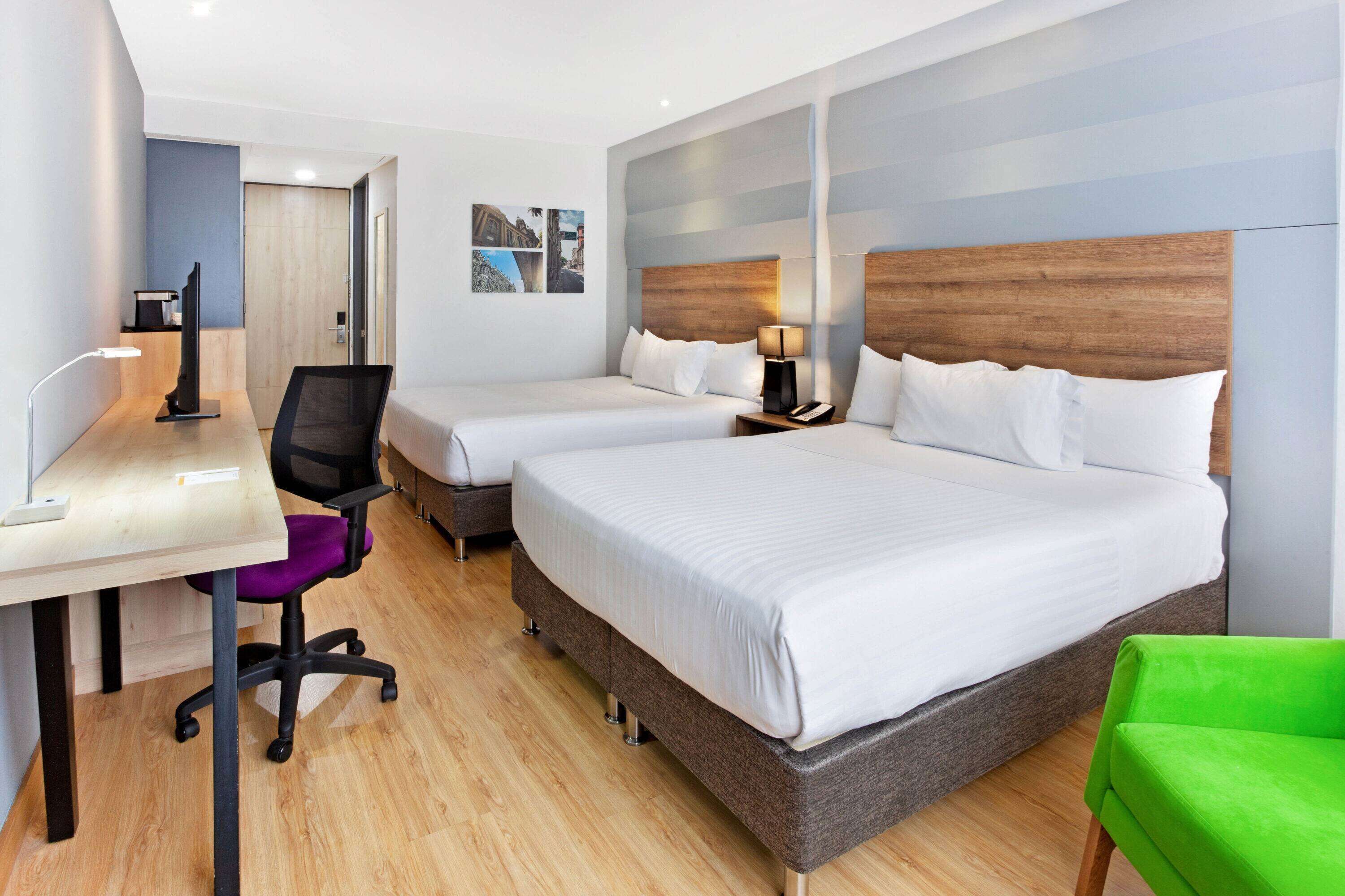A hotel room with two beds, a desk, a chair, and a TV.