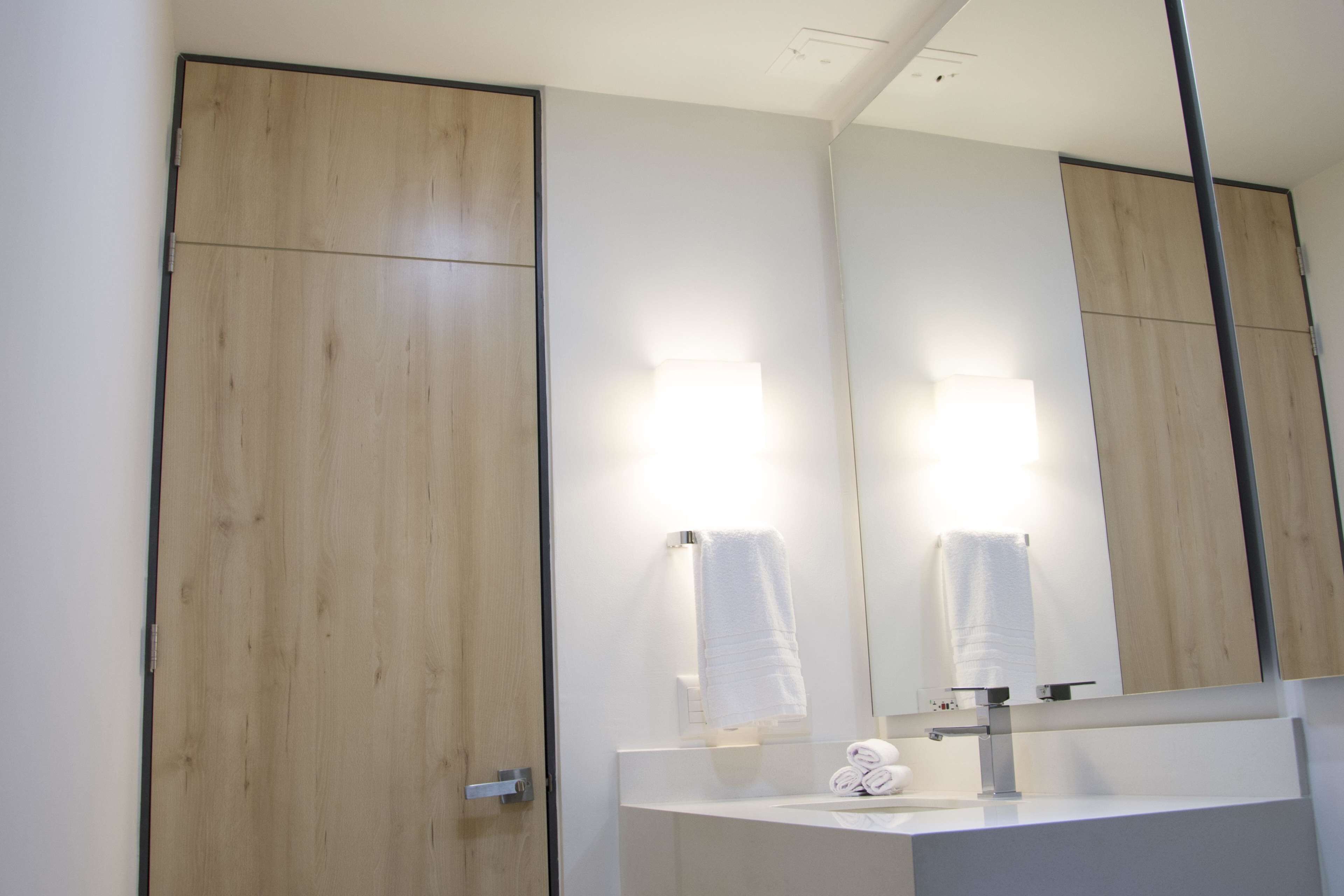 Un baño moderno con puerta de madera, un lavabo blanco y un espejo grande.