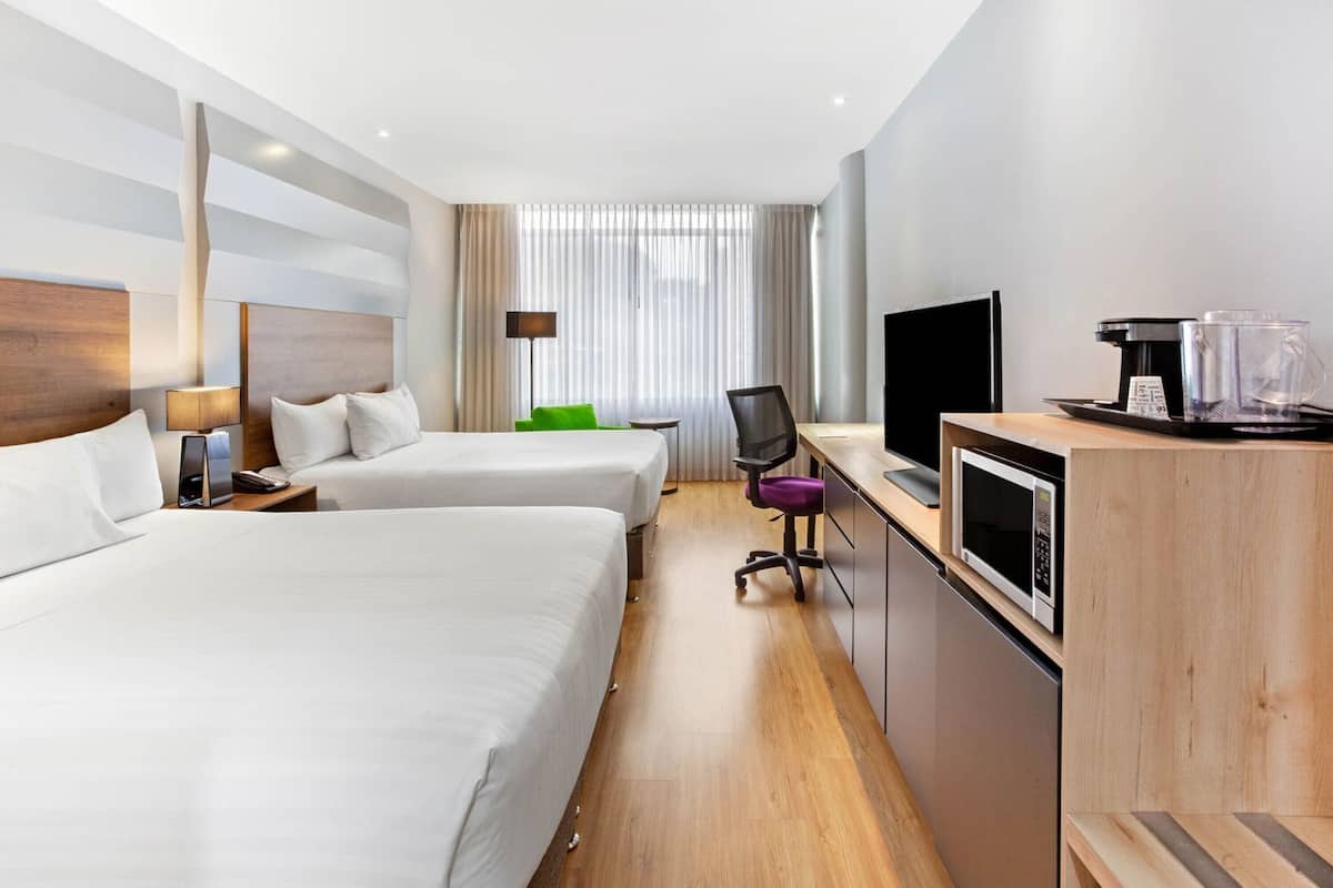 A hotel room with two beds, a desk with a TV, a coffee maker, and a microwave.