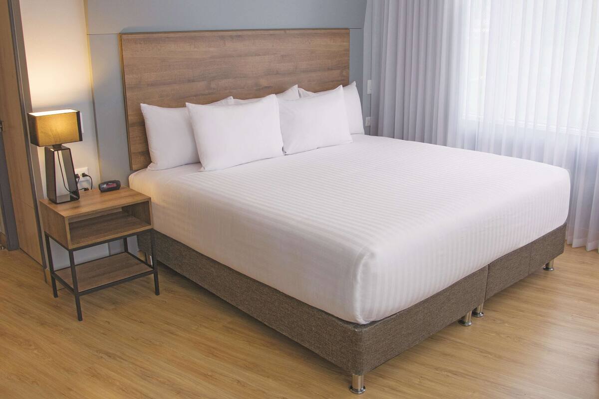 A large bed with a wooden headboard, white bedding, and a bedside table with a lamp.
