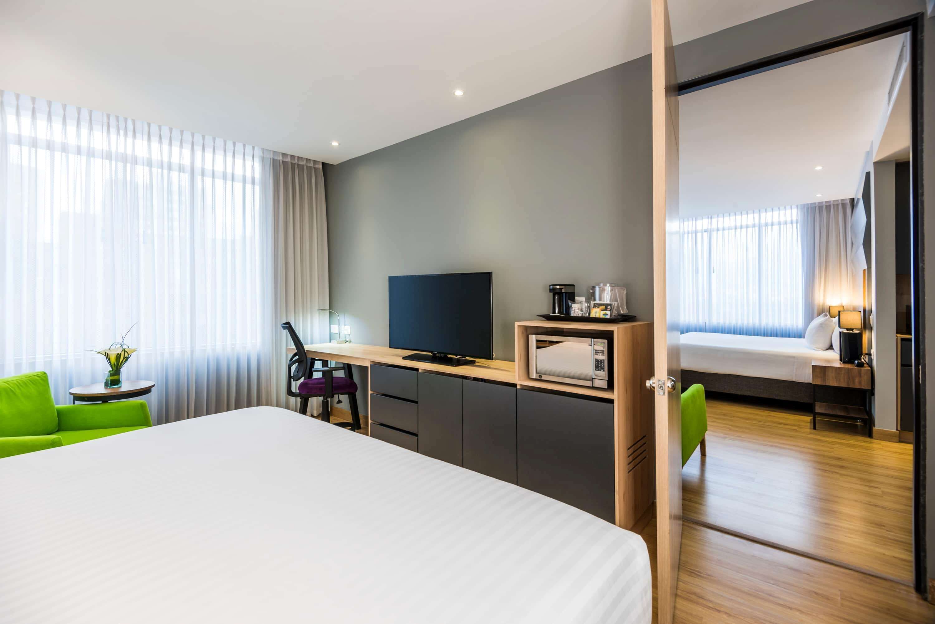 A modern hotel room with a large bed, a desk with a TV, a microwave, and a small table with a vase.