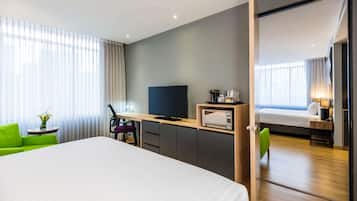 A modern hotel room with a large bed, a desk with a TV, a microwave, and a small table with a vase.