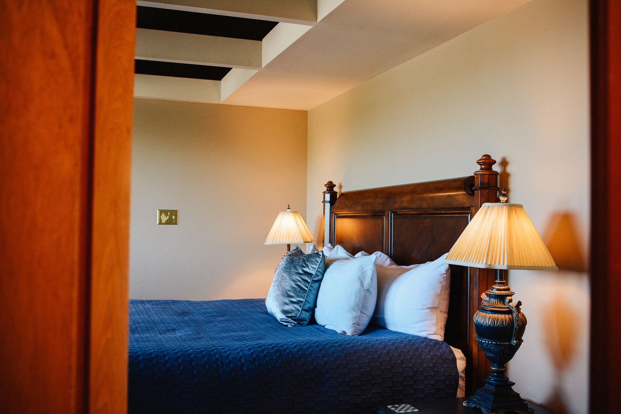 A bedroom with a wooden headboard, two bedside lamps, and a blue bedspread.