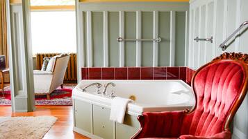 A bathroom with a bathtub, a red chair, and a window with curtains.